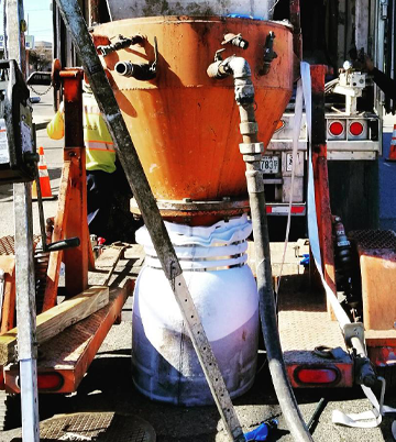 Hydro excavation equipment with a large orange tank and hoses, used for non-invasive pipe jetting services, positioned on a worksite.