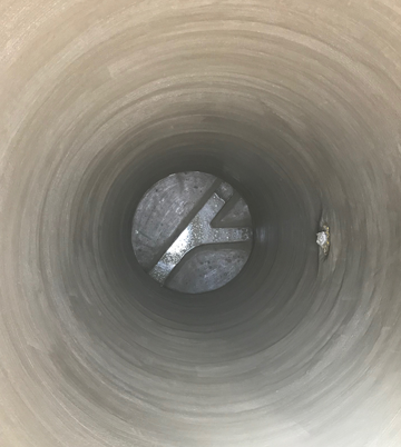 Inside view of a manhole showing smooth concrete walls and a metallic structure at the bottom, illustrating manhole rehabilitation services by Nor-Cal Pipeline Services.
