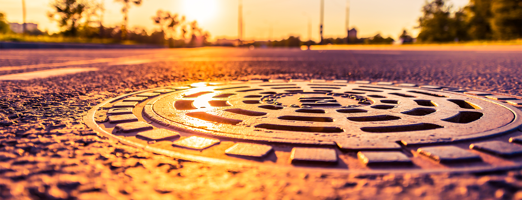 manhole cover sunset Manhole cover reflecting sunset light on asphalt road, symbolizing Nor-Cal Pipeline Services' focus on underground utility work and infrastructure.