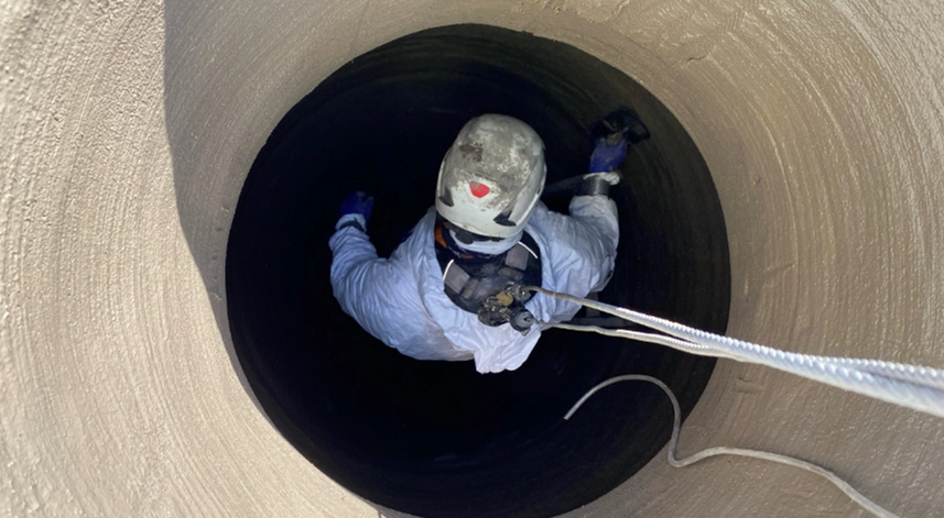 Worker in protective gear descending into a manhole for rehabilitation inspection, highlighting Nor-Cal Pipeline Services' manhole restoration services.