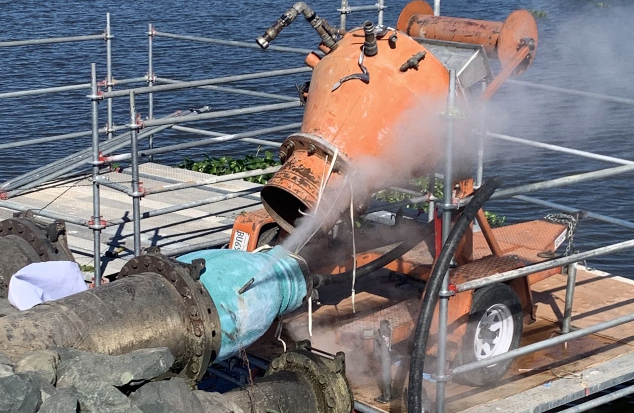 Hydro excavation equipment spraying water on a blue pipeline, illustrating trenchless CIPP lining process for pipeline rehabilitation.