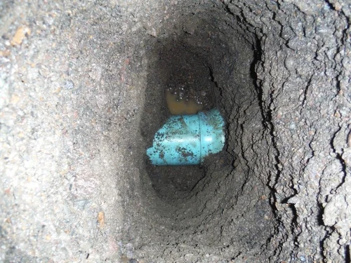 Underground utility excavation showing a blue pipe surrounded by dirt and water, illustrating subsurface utility engineering services.